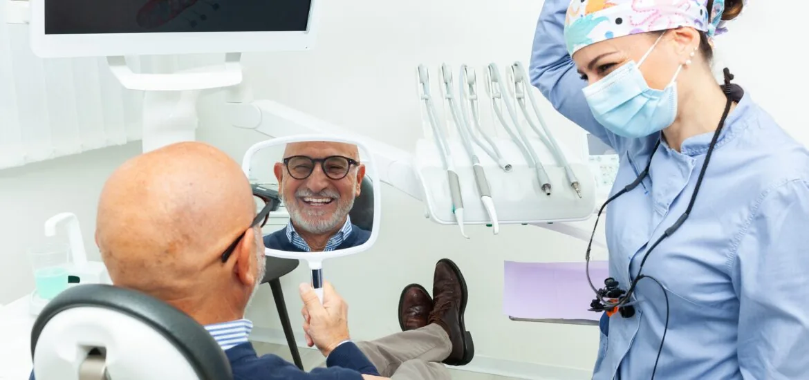 man smiling in mirror, happy with his new dental implants