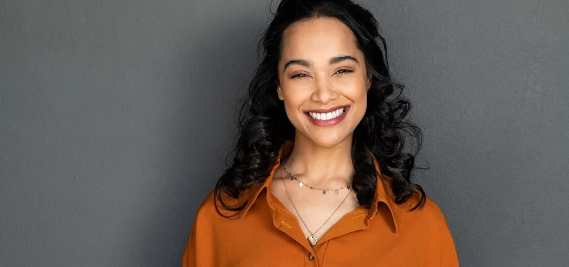 young woman smiling against a grey background, natural veneers